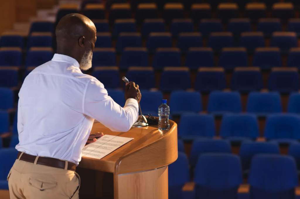 Speaker at lectern seen from behind at a lectern in front of an empty auditorium